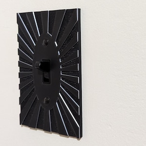 May include: Black light switch cover with a sunburst design. The switch is off.