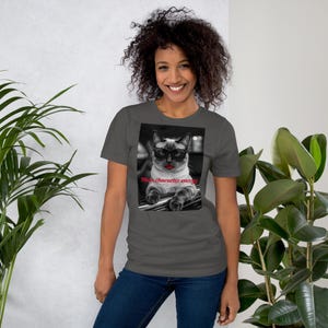 May include: A dark gray short-sleeve t-shirt featuring a black and white graphic of a cat wearing black-rimmed glasses and bright red lipstick. The text "Main character energy" is printed in red script below the cat's chin.
