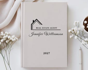 Op de afbeelding: Een lichtbeige hardcover planner met een zwarte afbeelding van een huisomtrek boven de tekst REAL ESTATE AGENT, de naam Jennifer Williamson in cursief schrift en het jaartal 2027 in een eenvoudig schreeflettertype.