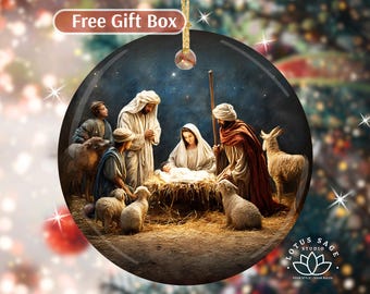 May include: Round Christmas ornament featuring a Nativity scene. The image depicts Mary, Joseph, baby Jesus, shepherds, and animals. The ornament has a gold-colored hanging loop and a "Free Gift Box" banner at the top.