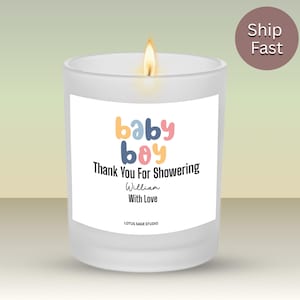 May include: A frosted glass candle with a lit wick, featuring a white label that reads baby boy Thank You For Showering William With Love and LOTUS SAGE STUDIO in black and colorful text. The candle emits a warm, glowing flame at the top.
