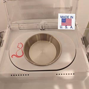 Puede incluir: Un comedero blanco para mascotas con tapa de plástico transparente. Cuenta con un cuenco de acero inoxidable y una silueta de gato rojo. Fabricado en EE. UU. El texto en la imagen dice "Not included feeder. Only sale plastic trim and bowl."