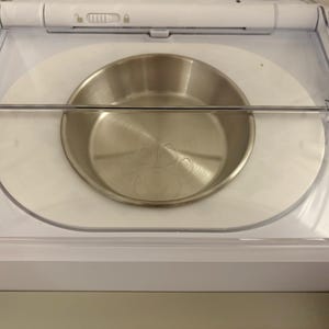 以下が含まれることがあります： ステンレス製のペットボウルが白いプラスチック容器の中に入っています。ボウルは丸く、つや消し金属仕上げです。透明なプラスチック製のガードがボウルの上に配置されています。容器には、ロック機構付きの白い蓋が付いています。