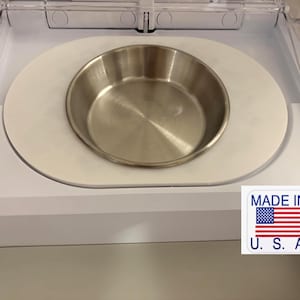 Può includere: Una ciotola per animali domestici in acciaio inossidabile inserita in un vassoio di plastica bianca. La ciotola è rotonda e ha una finitura metallica lucida. Il vassoio è inserito in un alloggiamento di plastica bianca. L'adesivo dice "MADE IN U.S.A."