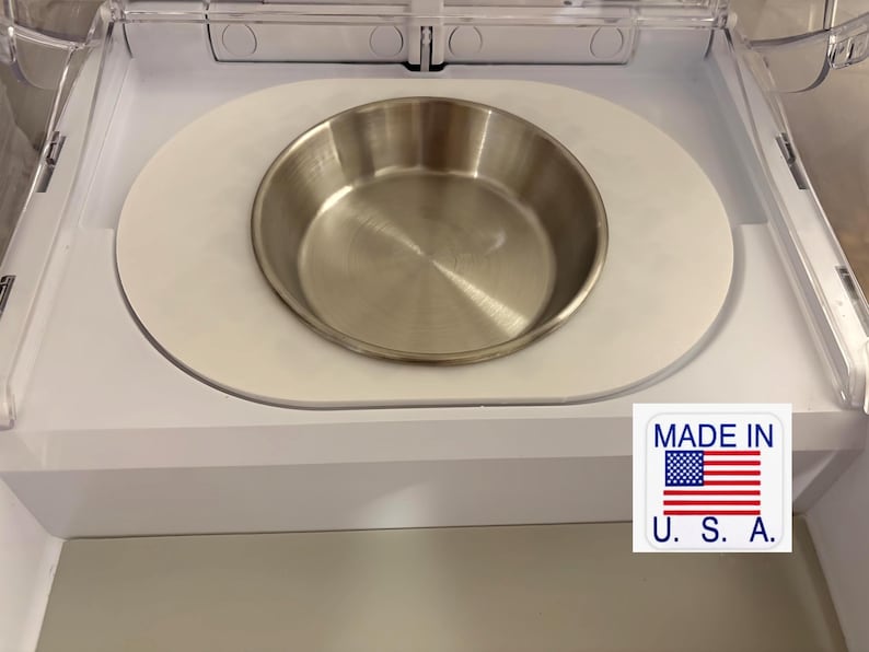 以下が含まれることがあります： 白いプラスチックトレイにセットされたステンレス製のペットボウル。ボウルは丸く、光沢のある金属仕上げです。トレイは白いプラスチックハウジングにセットされています。右下のステッカーには「MADE IN U.S.A.」と書かれています。