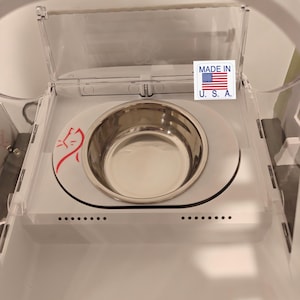 Puede incluir: Un comedero para mascotas de plástico blanco con un cuenco de acero inoxidable. El comedero tiene una tapa de plástico transparente y un logotipo de gato rojo. El texto "MADE IN U.S.A." es visible. El texto "Not included feeder. Only sale Plastic trim and bowl." también es visible.