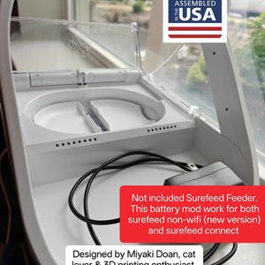 Può includere: Un alimentatore bianco per animali domestici con coperchio trasparente, progettato e assemblato negli Stati Uniti. L'alimentatore ha due scomparti per il cibo e un cavo di alimentazione. Il testo descrive la compatibilità del mod batteria.