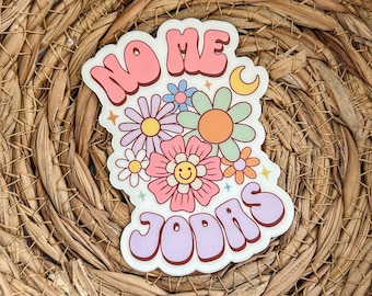 May include: A sticker with the text "NO ME JODAS" in a retro font with a pink background and a design of flowers and stars.