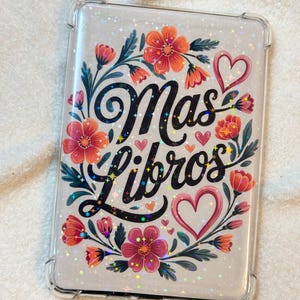 May include: A clear phone case with a floral design and the text "Mas Libros" in black lettering. The design features red, pink, and green flowers with a glittery background.