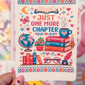 May include: A cross-stitch design featuring the text "JUST ONE MORE CHAPTER" with a globe, books, a coffee cup, and other book-related elements. The design is in shades of pink, blue, orange, and white.