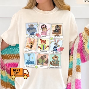 May include: An ivory t-shirt featuring a grid of nine polaroid-style frames, each containing a cartoon character with their name printed below. The characters include Chief Bogo, Judith, Mr. Big, Finnick, Nick Wilde, Judy Hopps, Gary de'snack, Flash, and Nibbles Maplestick, accented by small colourful stars and mouse-ear shapes.