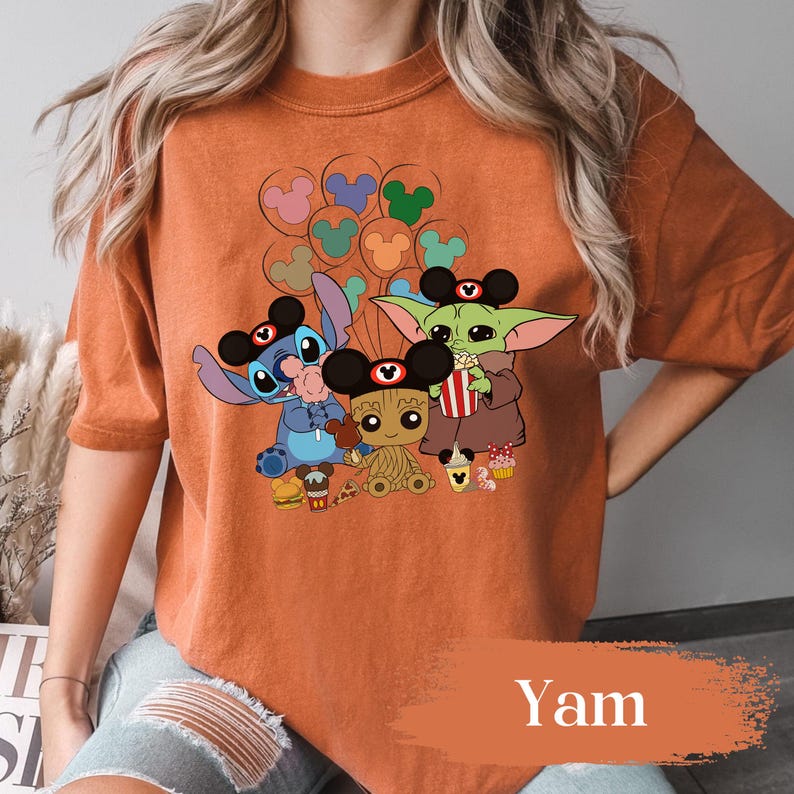 May include: Orange t-shirt with a graphic of Stitch, Baby Yoda, and Groot wearing Mickey Mouse ears. The characters are holding snacks and balloons. The word "Yam" is printed at the bottom of the shirt.