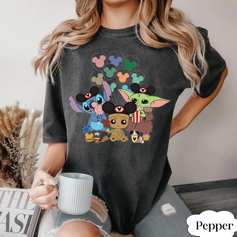May include: Dark grey t-shirt with cartoon characters Stitch, Baby Groot, and Grogu, each wearing Mickey Mouse ears. The design includes Mickey Mouse balloon graphics and food items. The word "Pepper" is in the bottom right corner.