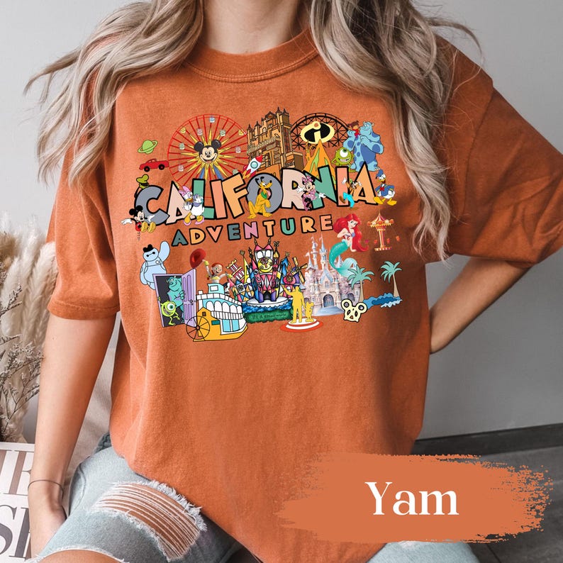 May include: An orange-colored t-shirt featuring the words "California Adventure" with various cartoon characters and amusement park imagery. The shirt has a relaxed fit and short sleeves, perfect for casual wear.