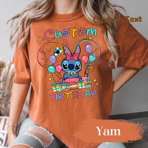 May include: Orange t-shirt with a colorful graphic featuring a cartoon character, balloons, and the words "Custom Birthday." The design includes a cake, presents, and stars. The shirt is a solid orange color.