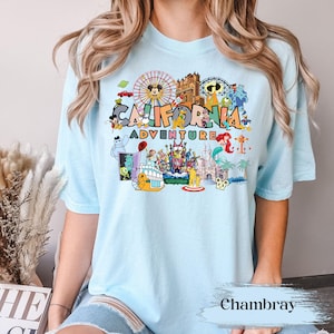 May include: Light blue t-shirt featuring a colorful graphic of the California Adventure theme park. The design includes a Ferris wheel, cartoon characters, and the words "CALIFORNIA ADVENTURE". The shirt is made of soft material.
