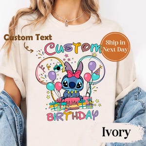 May include: Ivory-colored t-shirt featuring a cartoon character with a birthday cake, balloons, and the word "BIRTHDAY". The shirt has the text "Custom" above the character. The design includes a blue character with a pink bow.