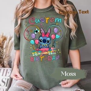 May include: Moss green t-shirt featuring a colorful graphic of a cartoon character with a birthday cake, balloons, and gifts. The words "Custom Birthday" are displayed in a playful font. The shirt is made of a soft material.