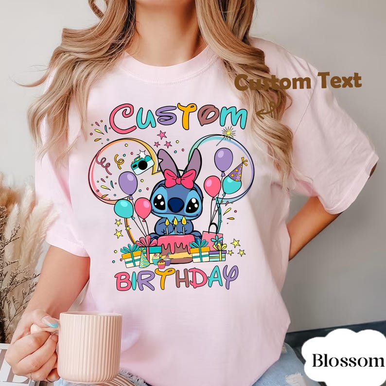 May include: A light pink t-shirt featuring a cartoon character with a birthday cake, balloons, and the words "Custom Birthday." The design includes colorful accents and stars, creating a festive look.