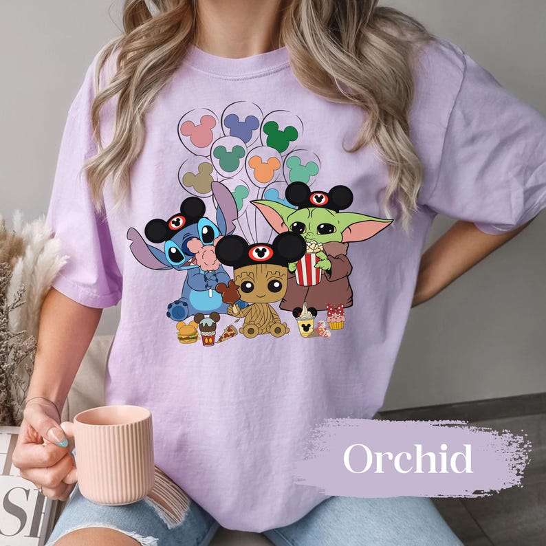 May include: Lilac t-shirt with a graphic of Stitch, Baby Groot, and Grogu wearing Mickey Mouse ears. The characters are holding balloons and snacks. The word "Orchid" is printed at the bottom.