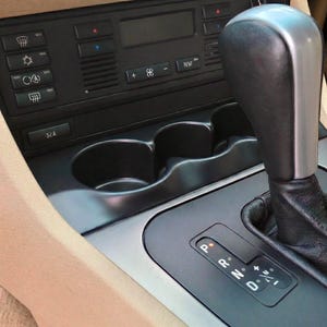 May include: A white ceramic mug with a black handle and the text "But first, coffee" in a handwritten style. The mug is on a white surface. The mug is 10 cm tall.