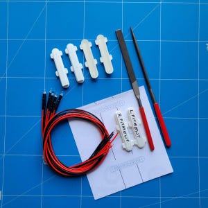 Może przedstawiać: Widok z góry na różne materiały rzemieślnicze na niebieskiej powierzchni kratki. Widoczne są białe plastikowe elementy, wiązka czerwonych i czarnych przewodów, metalowy pilnik i spiczaste narzędzie. Na kartce papieru widnieje napis "R FITMENT" i "L FITMENT".