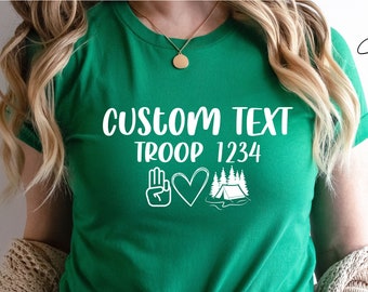 May include: Green t-shirt with white text that says "CUSTOM TEXT TROOP 1234" and a peace sign, heart, and tent graphic.