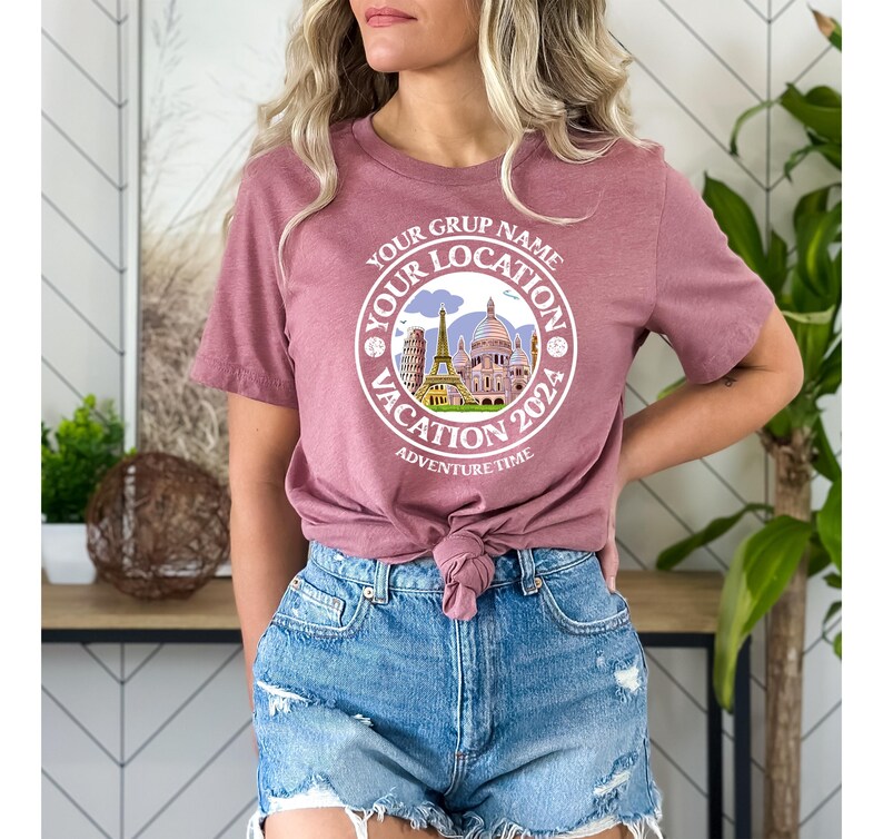 K&ouml;nnte beinhalten: Ein mauvefarbenes T-Shirt mit einem wei&szlig;en Kreis-Motiv, das eine Stadtlandschaft und den Text "Your Grup Name Your Location Vacation 2024 Adventure Time" zeigt.