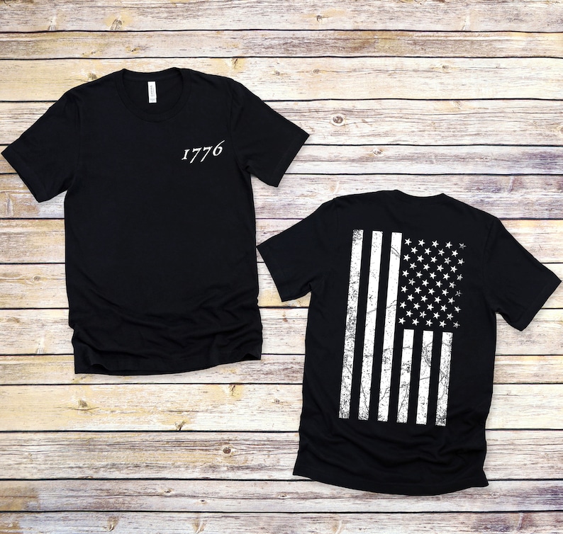 K&ouml;nnte beinhalten: Schwarzes T-Shirt mit der Zahl 1776 auf der Vorderseite und einem verwitterten amerikanischen Flaggenmuster auf der R&uuml;ckseite.
