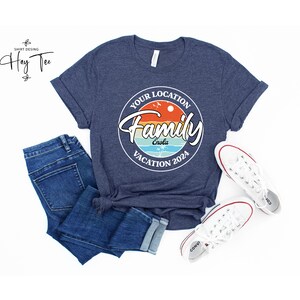 K&ouml;nnte beinhalten: Ein marineblaues T-Shirt mit einem wei&szlig;en Kreis-Motiv, auf dem "Your Location Family Vacation 2024" mit einem Sonnenuntergang und Palmen steht. Der Text "Enola" befindet sich innerhalb des Kreises.