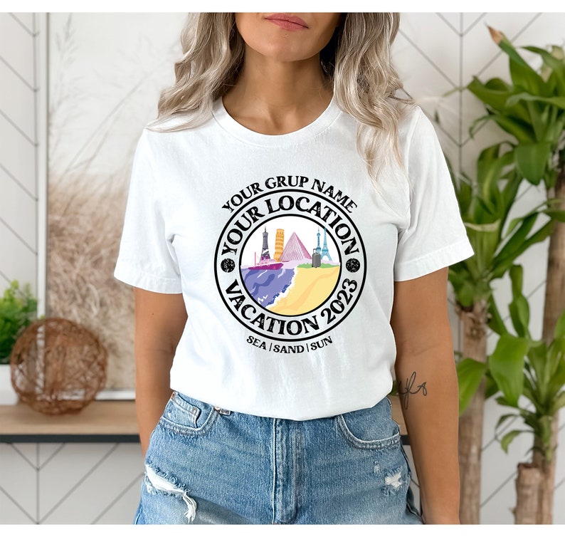 May include: White t-shirt with a black circle graphic that says "Your Group Name Your Location Vacation 2023 Sea | Sand | Sun". The graphic features a colorful illustration of a beach scene with buildings and a boat.