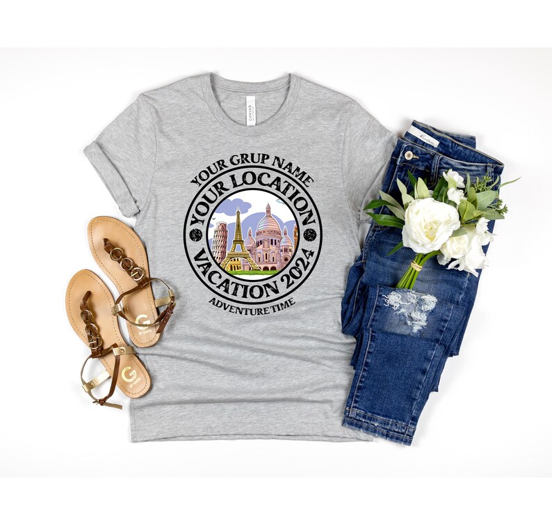 K&ouml;nnte beinhalten: Graues T-Shirt mit einem schwarzen Kreis-Motiv, auf dem "Your Grup Name Your Location Vacation 2024 Adventure Time" steht. Das Motiv zeigt eine Stadtlandschaft mit Geb&auml;uden und blauem Himmel.