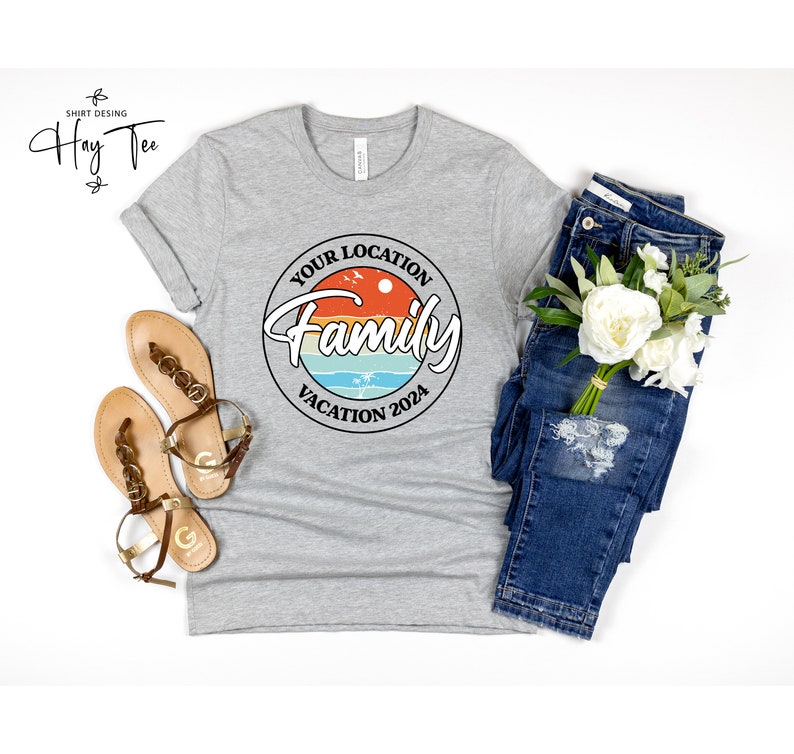 K&ouml;nnte beinhalten: Ein graues T-Shirt mit einem runden Design, das einen Sonnenuntergang, Palmen und den Text "Your Location Family Vacation 2024" zeigt.