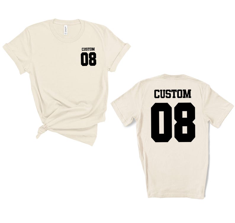 May include: Two cream-coloured t-shirts, one front and one back view. Each shirt has the word "CUSTOM" above the number "08" in black block letters. The front of the shirt has the text on the upper left chest. The back of the shirt has the text centered.