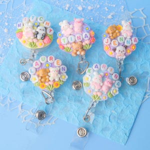 May include: Five colorful, personalized badge reels with cute animal charms. Each reel features a different name: Mitch, Tina, Jenna, Lauren, and Karina. The charms include bears, bunnies, and a penguin.