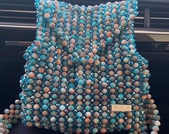 May include: A turquoise and brown beaded handbag with a silver clasp. The bag has a long beaded strap.