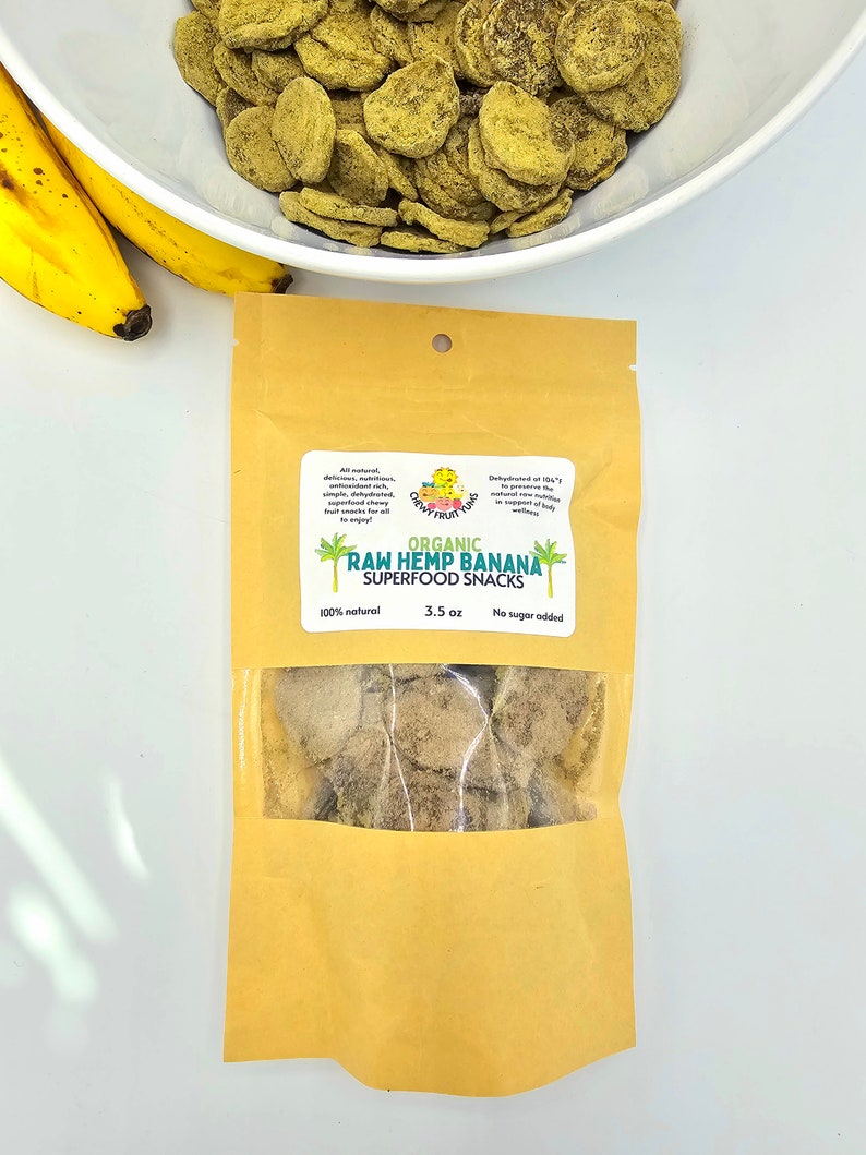 May include: A brown paper bag with a clear window showing a small amount of dried, light brown banana chips. The bag has a label that reads "ORGANIC RAW HEMP BANANA SUPERFOOD SNACKS 100% natural 3.5 oz No sugar added".