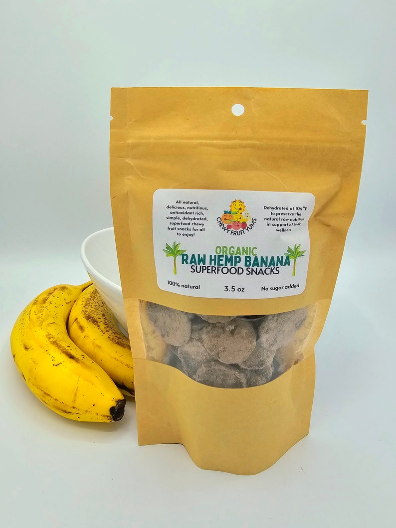 May include: A brown paper bag with a clear window showing organic raw hemp banana superfood snacks. The bag is labeled with the brand name "Chewy Fruit Yum's" and the product name "Organic Raw Hemp Banana Superfood Snacks". The bag also states that the product is 100% natural, 3.5 oz, and no sugar added.