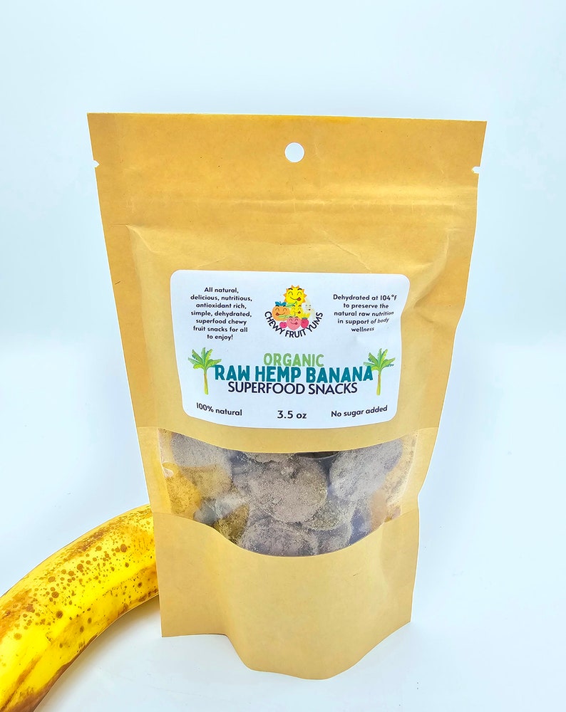 May include: A brown paper bag with a clear window showing organic raw hemp banana superfood snacks. The bag has a green logo with the text "Chewy Fruit Yums" and the text "Organic Raw Hemp Banana Superfood Snacks". The bag also has the text "100% natural", "3.5 oz", and "No sugar added".