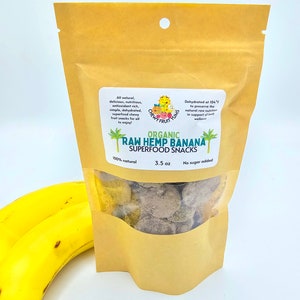 May include: A brown paper bag with a clear window showing organic raw hemp banana superfood snacks. The bag is labeled with the text "Chewy Fruit Yums" and "Organic Raw Hemp Banana Superfood Snacks". The bag is 3.5 oz and contains no sugar added.