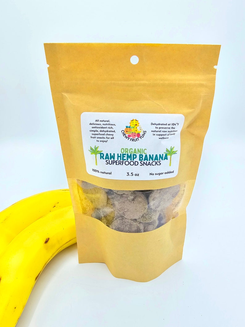 May include: A brown paper bag with a clear window showing organic raw hemp banana superfood snacks. The bag is labeled with the text "Chewy Fruit Yums" and "Organic Raw Hemp Banana Superfood Snacks". The bag is 3.5 oz and contains no sugar added.