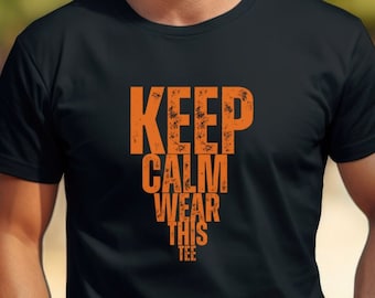 Puede incluir: Una camiseta negra con un gráfico naranja que dice "Keep Calm Wear This Tee".