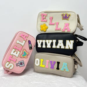 May include: Four different cosmetic bags with personalized names. The bags are in pink, beige, black, and white with colorful letters and embellishments. The names on the bags are Stella, Olivia, Vivian, and Ella.