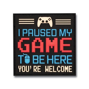May include: Black square patch with the text "I PAUSED MY GAME TO BE HERE YOU'RE WELCOME". The text is in white, blue, and red. A white game controller and mouse are at the top and bottom of the patch.