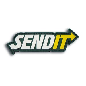 May include: A rectangular patch with the text "SEND IT" in white, bold letters. The text is inside a green rectangle with a yellow arrow pointing right. A white arrow points left. The patch has a black border.