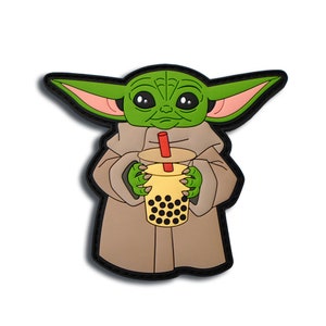 May include: A green cartoon character with large ears and a tan robe, holding a yellow bubble tea with a red straw. The character is outlined in black, with a black border. The image is on a white background.