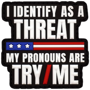 May include: A rectangular black morale patch with white raised lettering that reads I IDENTIFY AS A THREAT. Below this, a horizontal graphic features a blue section with three white stars and red and white stripes. The text MY PRONOUNS ARE TRY/ME follows.