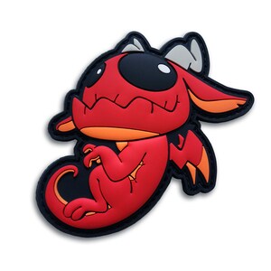 May include: A red cartoon dragon patch with black and orange accents. The dragon has large black eyes, a toothy grin, and orange wings. The patch is outlined in black.