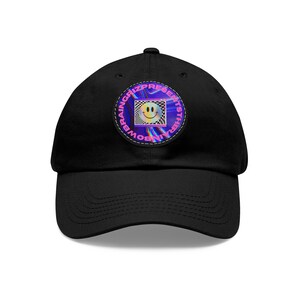 May include: Black baseball cap with a curved brim. The cap features a circular patch with a smiley face inside a checkered pattern. The patch is surrounded by the text "BRAINGRIZ PRESENTS RAINBOWSISTER".