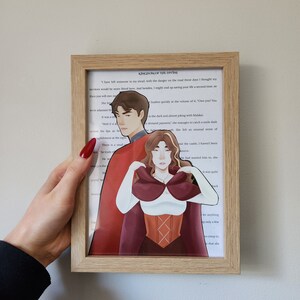 May include: A framed illustration of a couple in a fantasy setting. The man is wearing a red cloak and the woman is wearing a red dress with a white bodice. The text in the image reads "Kingdom of the Divine".